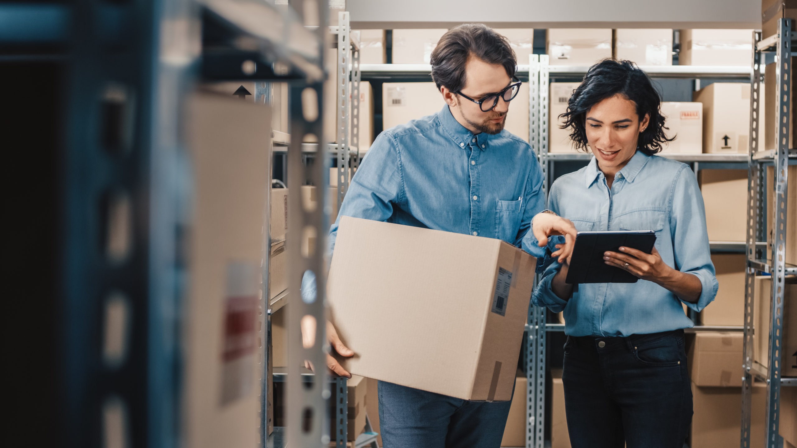 Female Inventory Manager Shows Digital Tablet Information to a Worker Holding Cardboard Box, They Talk and Do Work. In the Background Stock of Parcels with Products Ready for Shipment. 鼎天国际官方网站图片